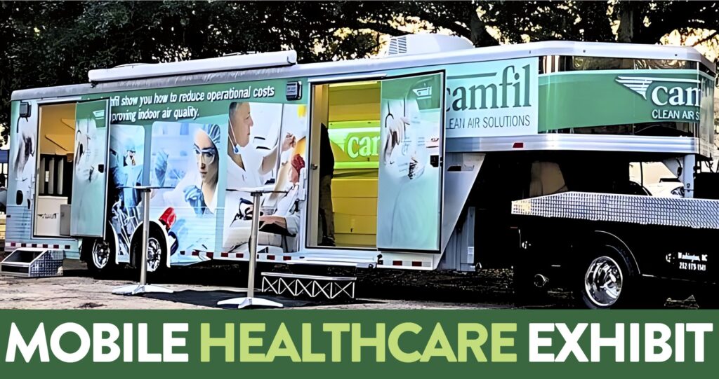 Mobile exhibit showcases latest tech in air filtration for healthcare. A steel trailer with a wrap on it. The wrap has pictures of a female medical professional preparing some medicine and another of a mail doctor with a mask caring for a patient. The doors to the trailer are open and you can see a Camfil sign that is glowing in light green. 
